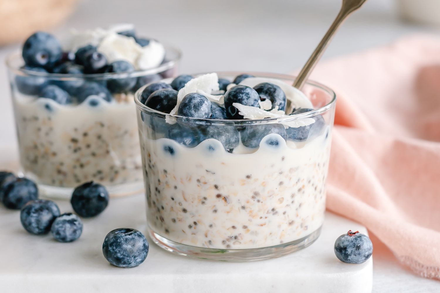 A serving of overnight oats topped with blueberries and a spoon in a glass container