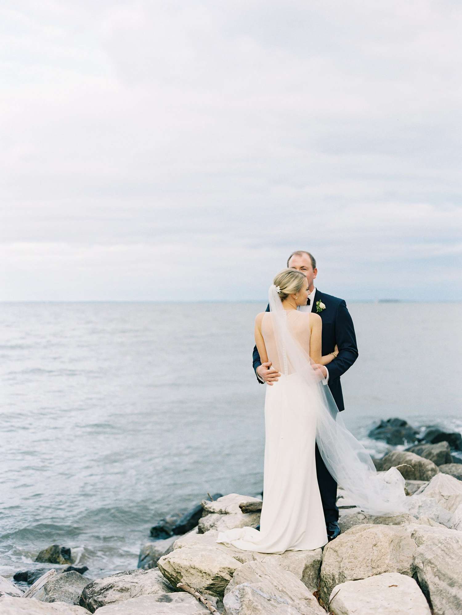beach wedding dresses couple standing on rocks by the water