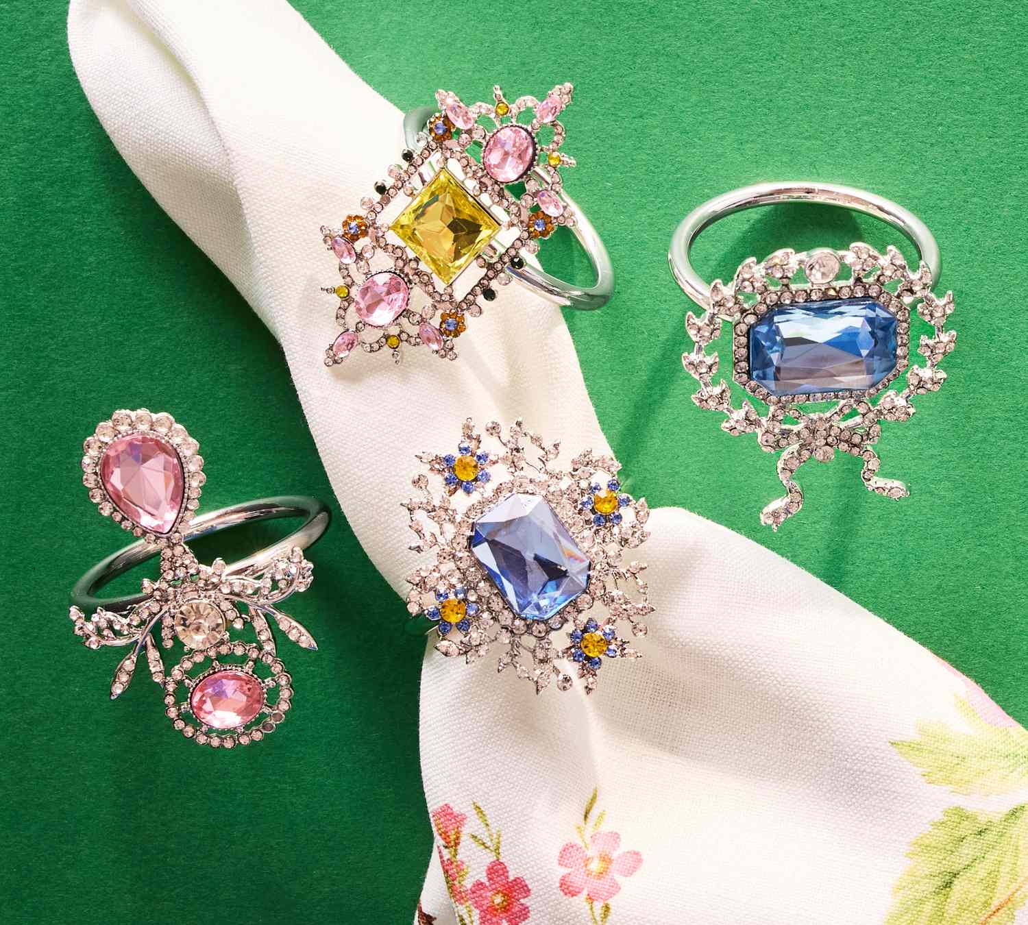 Ornate rings set against a green background, displayed alongside a floral-patterned cloth