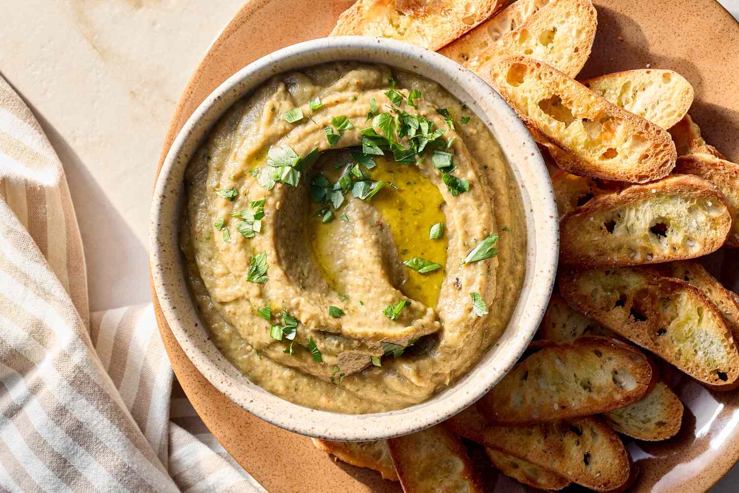 Bowl of eggplant dip garnished with herbs surrounded by pieces of toasted bread