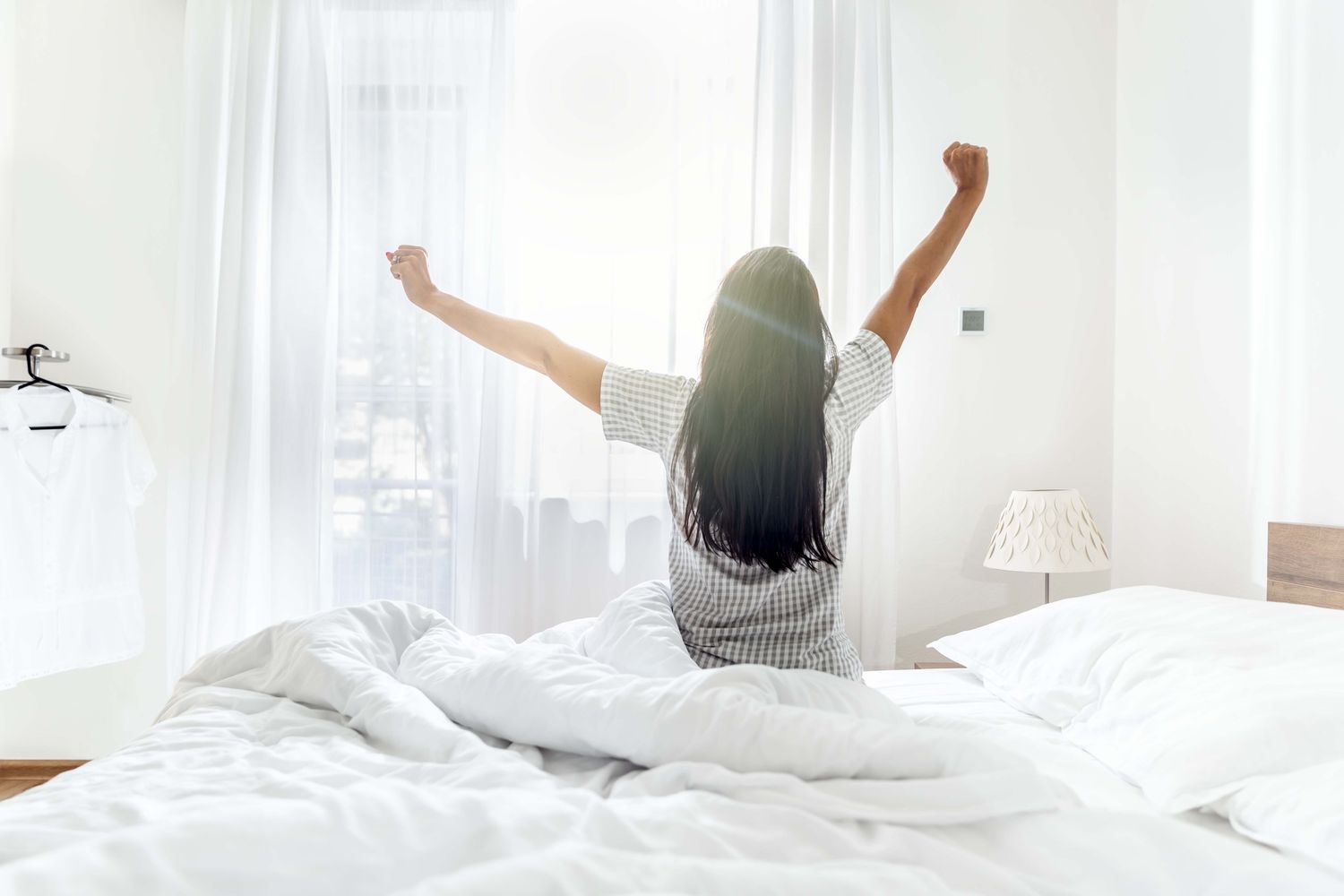 Person stretching on a bed in a bright room with curtains