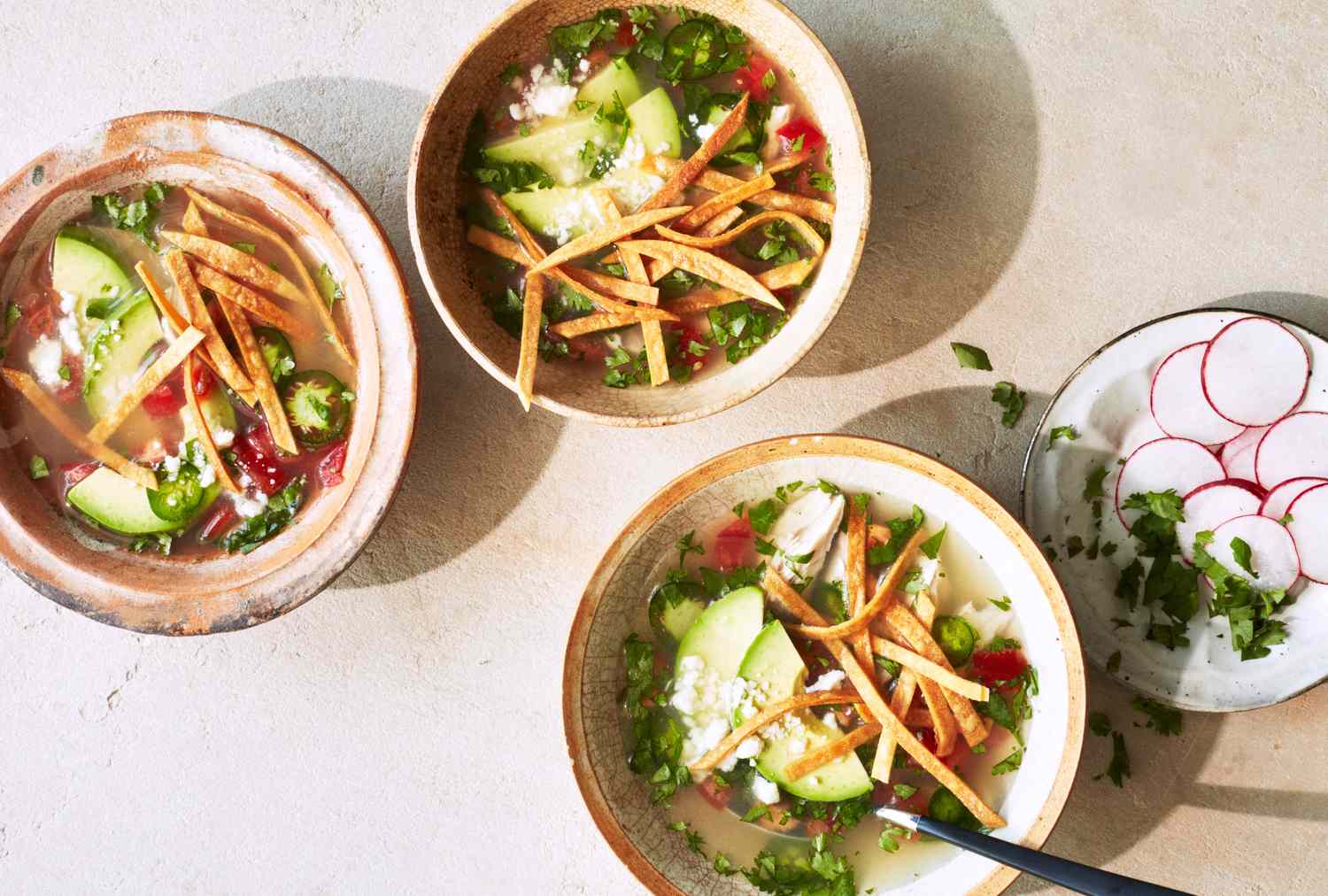 Tortilla soup served in three bowls garnished with avocado slices fried tortilla strips and a side dish of radish slices