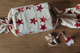 A fabricwrapped gift with a star pattern resting on a wooden surface accompanied by ribbon and a small tag