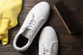 White shoes with cleaning tools including a yellow cloth and a brush on a wooden surface