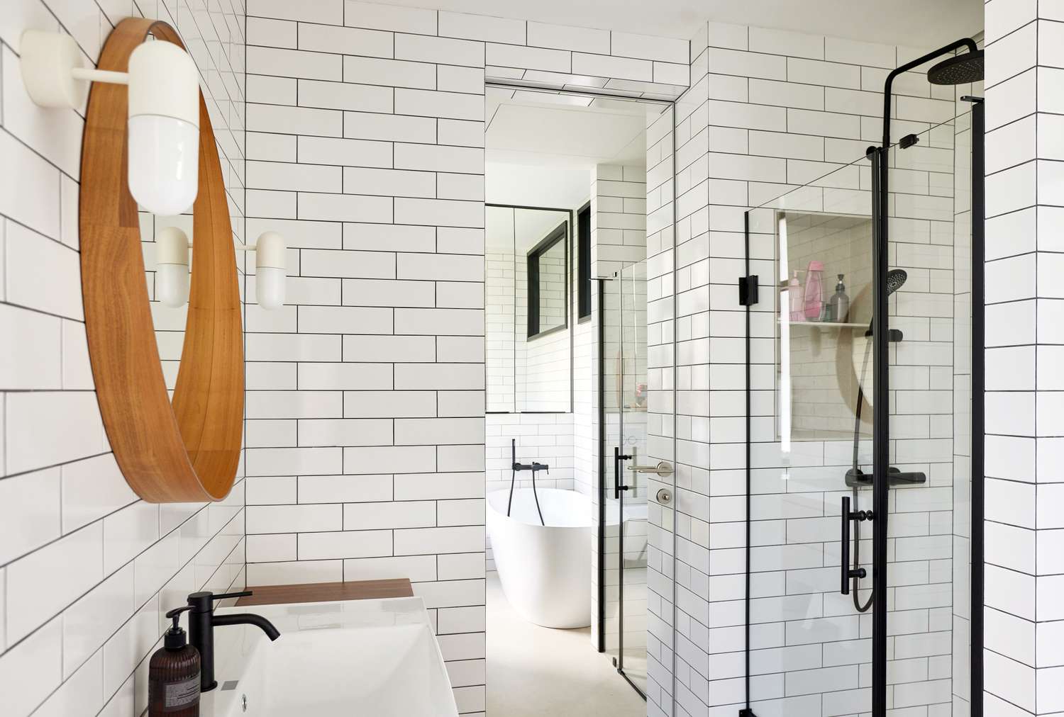 Modern bathroom with tiled walls a glass shower and round wooden mirror