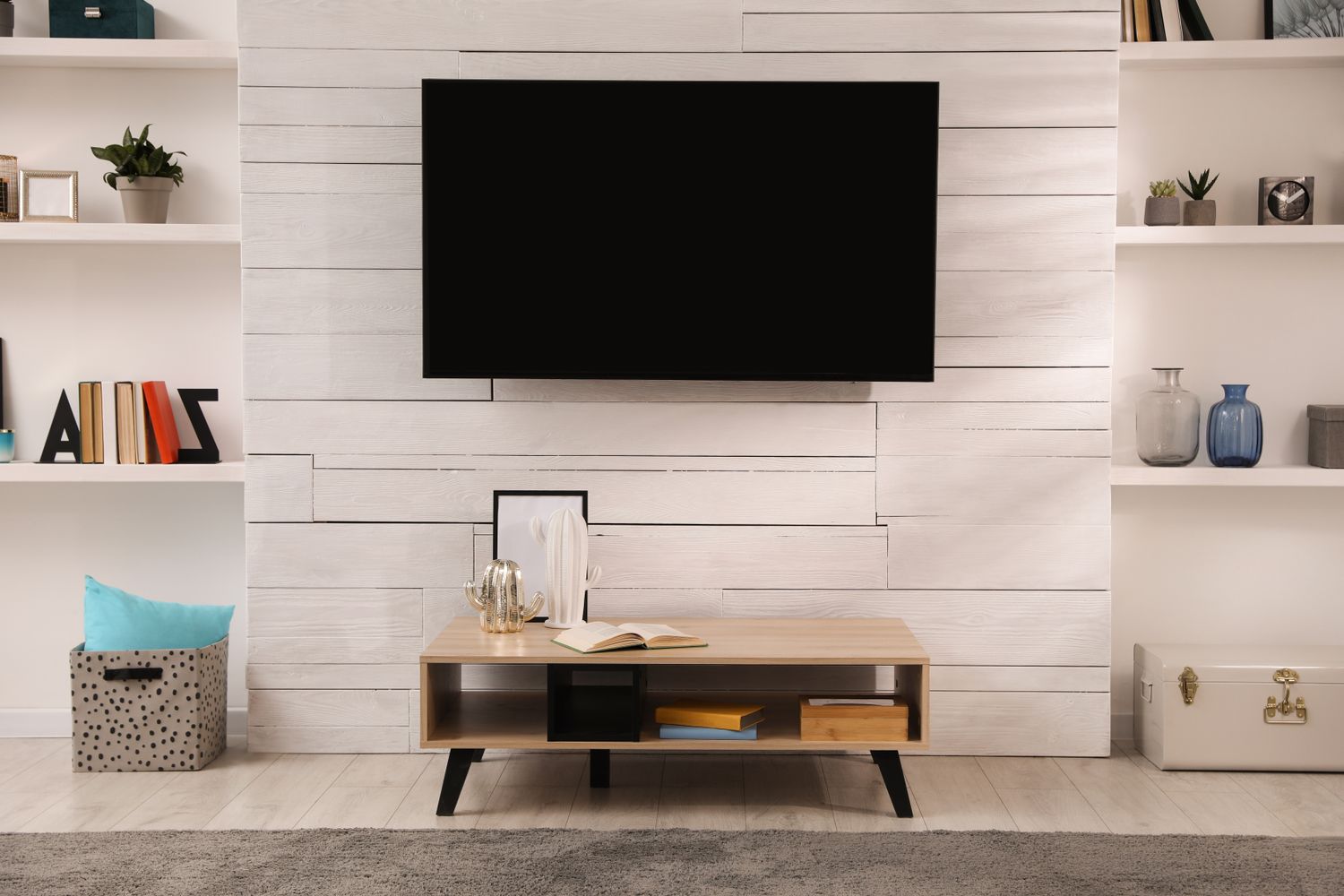 Living room setup featuring a wallmounted television a wooden console table with books and shelving with various items