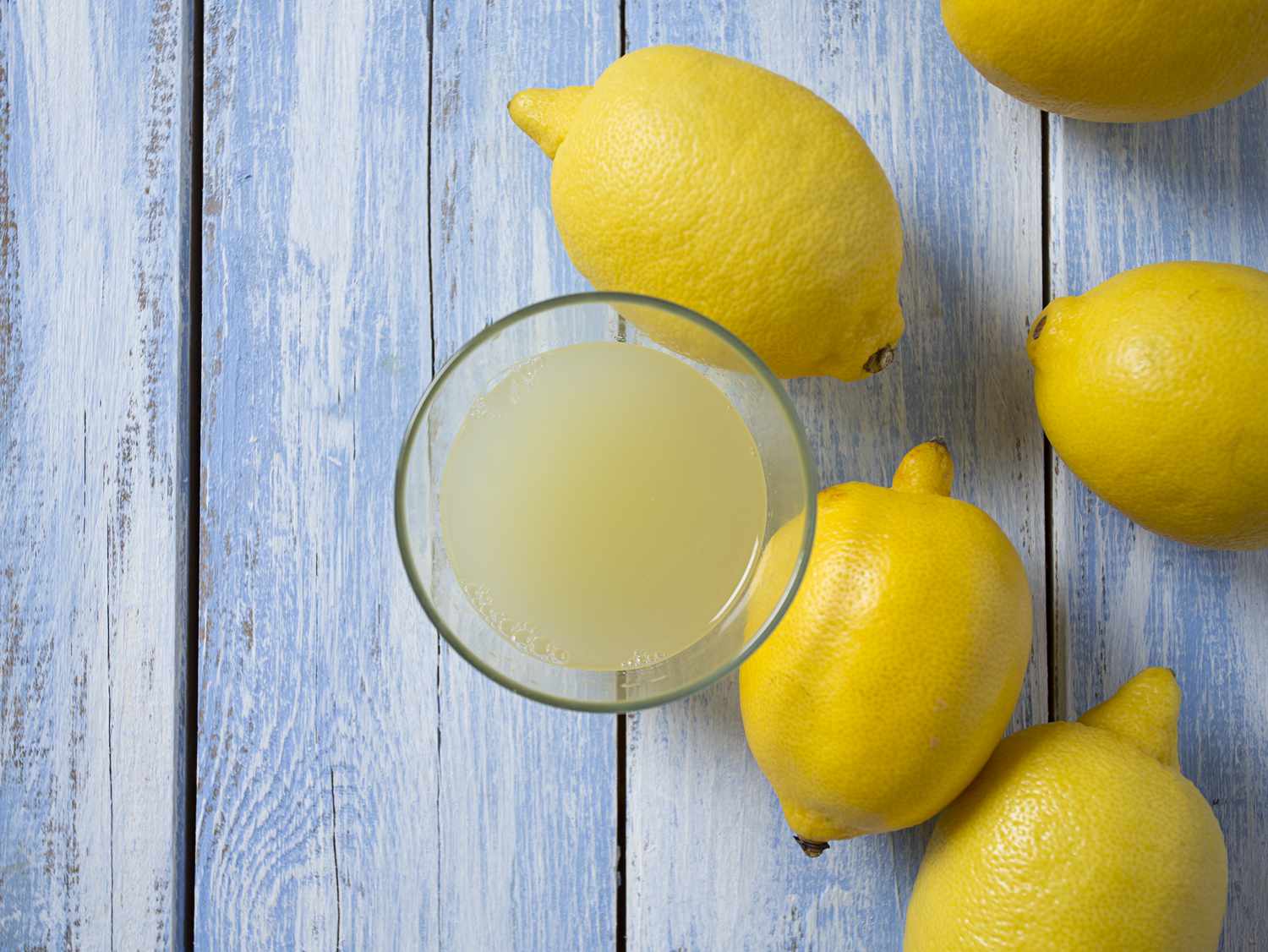 lemons and glass bowl of lemon juice on blue wood surface
