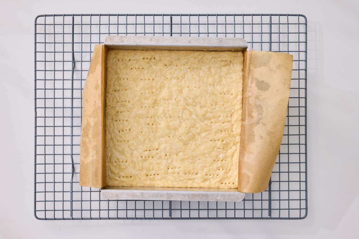 Baked crust in a square pan lined with parchment paper cooling on a wire rack