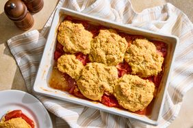 Baking dish filled with tomato cobbler layered tomatoes and biscuit topping placed on a striped kitchen towel