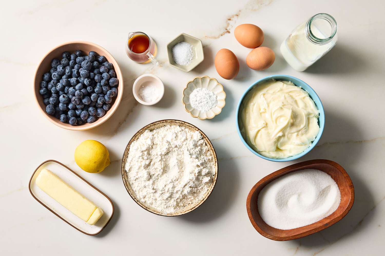 Ingredients for baking including flour eggs sugar butter blueberries lemon and more on a counter