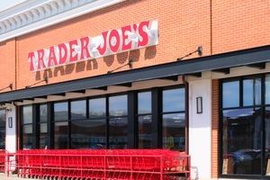 View of the Trader JOE'S logo sign on a supermarket building facade with rows of grocery carts. 