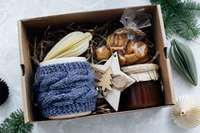 Gift box with items including a knitted cup holder a jar of preserves a starshaped ornament and treats in packaging