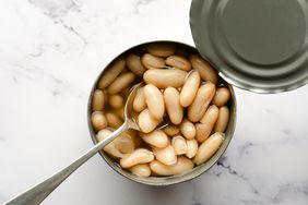 An open can of white beans with a spoon on a marble surface