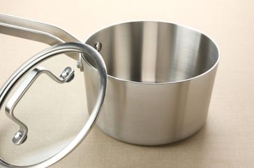 A stainless steel saucepan with a glass lid beside it