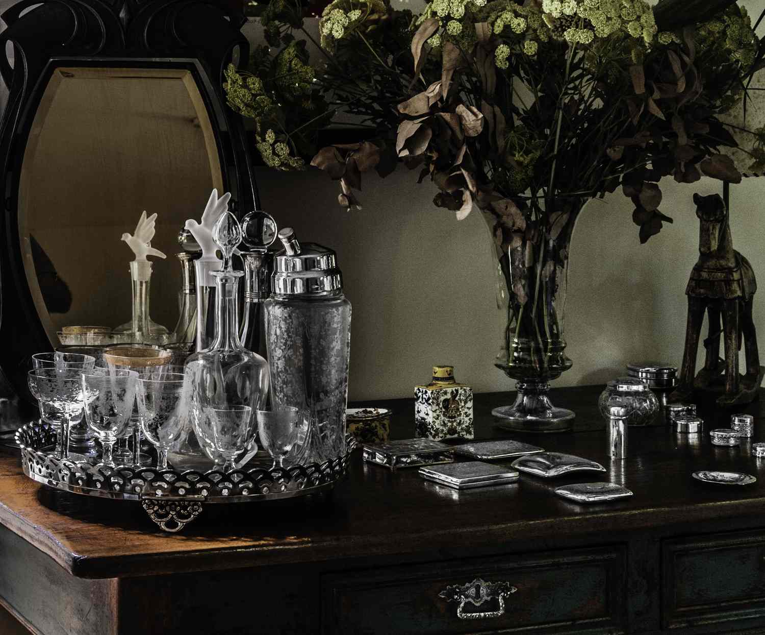 An arrangement of glassware, a mirror, and a bouquet of flowers on a table