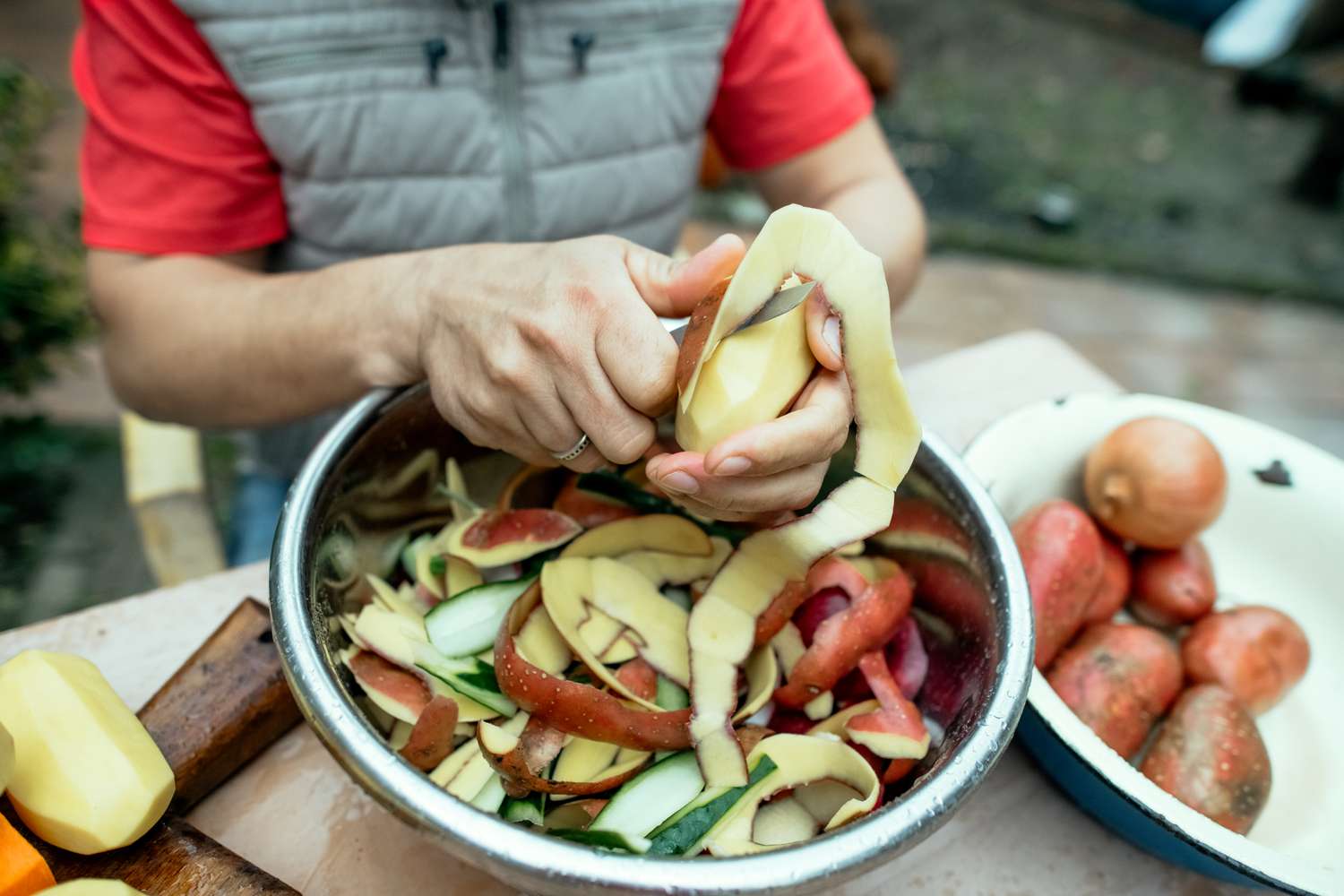 Person peeling potatoes into a bowl of vegetable scraps