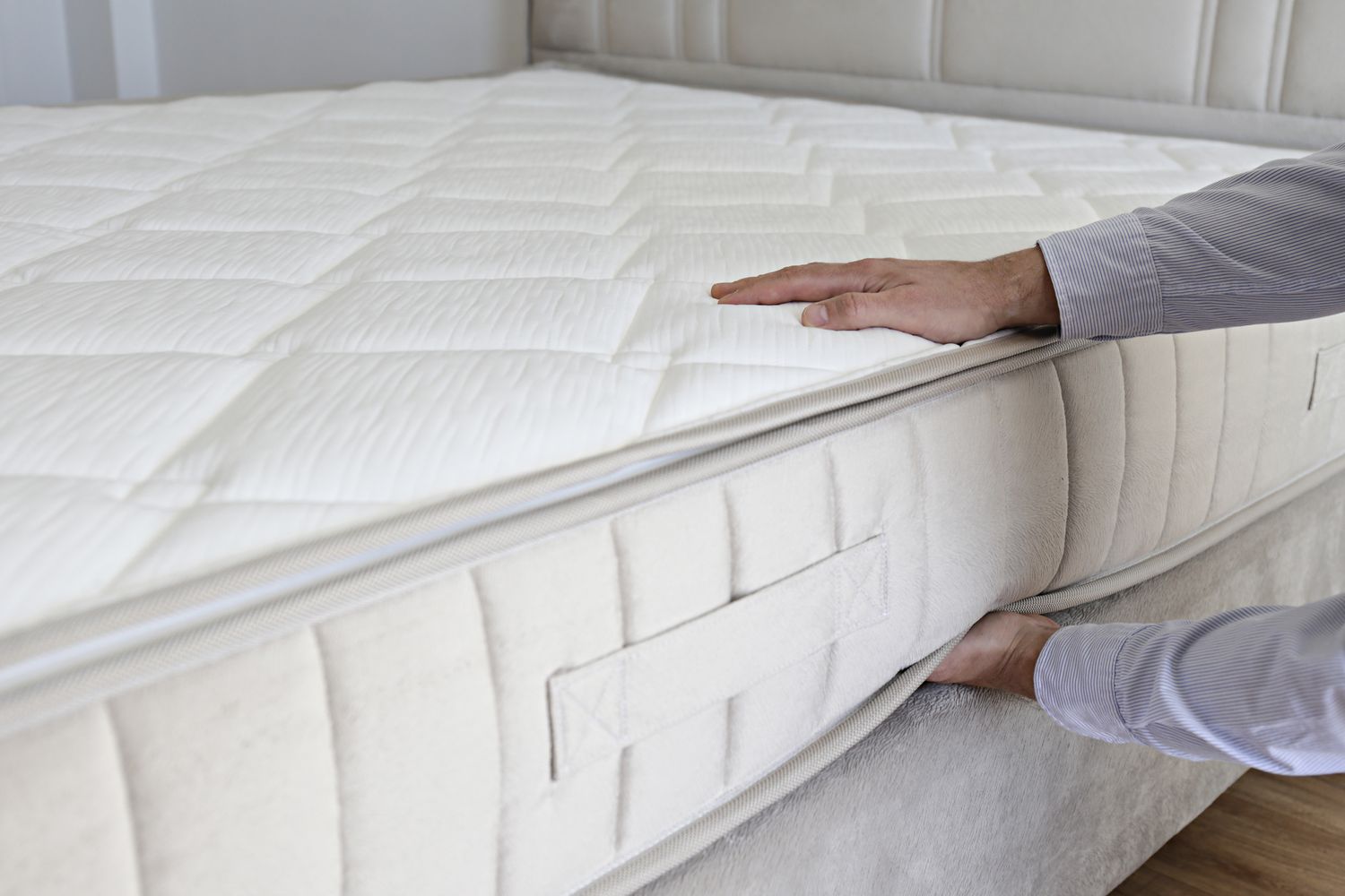 Hands adjusting the corner of a mattress on a bed frame