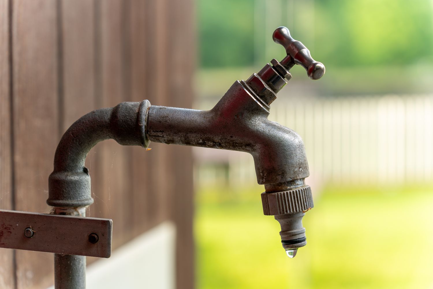 An outdoor faucet with a single drip of water hanging at its outlet