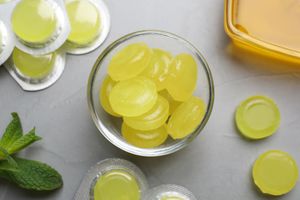 A bowl filled with round medicinal lozenges surrounded by blister packs and mint leaves