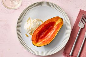 A plate with roasted papaya and a scoop of ice cream placed on a pink background with cutlery nearby