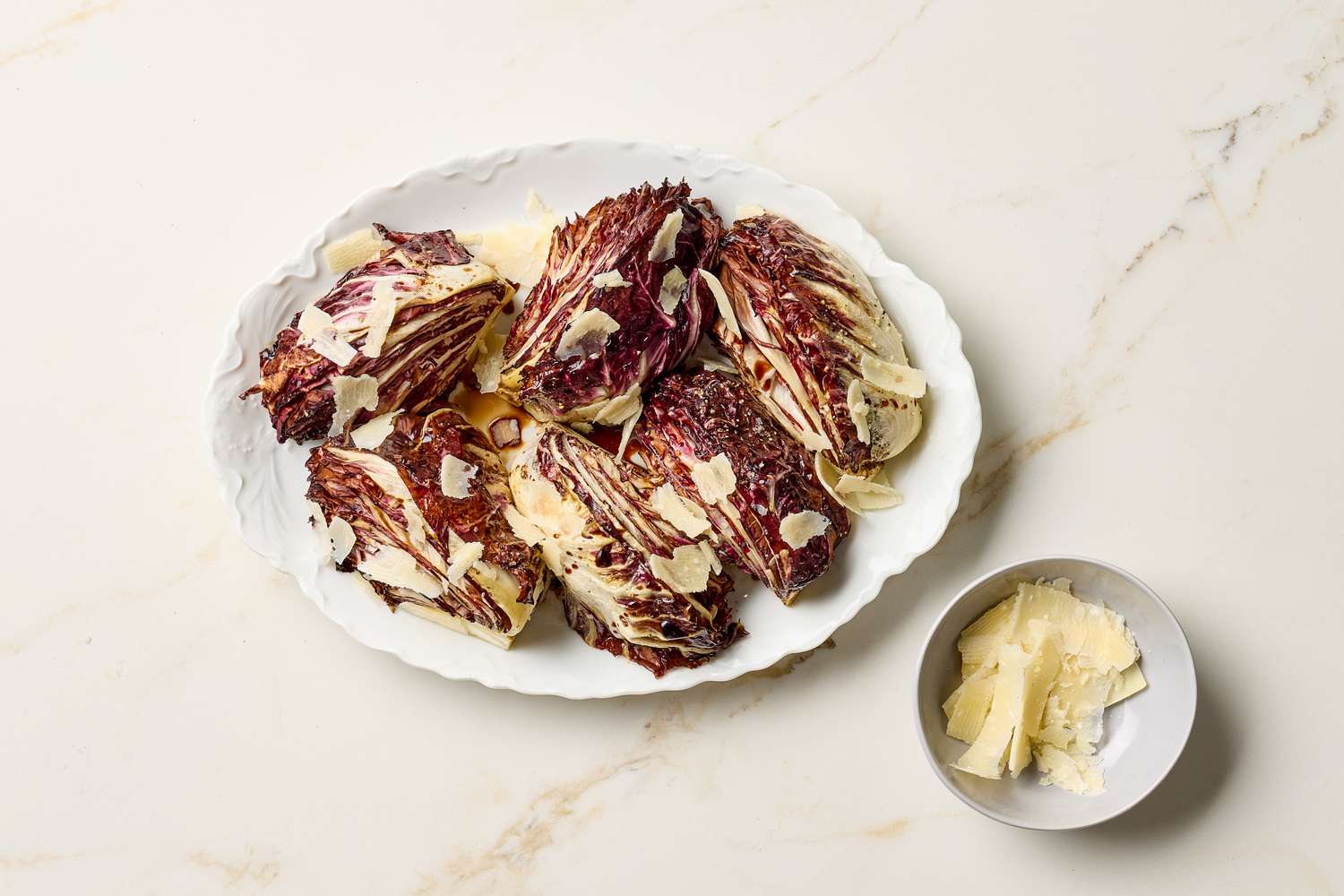 Plate of roasted radicchio with shaved cheese on top small bowl of additional cheese shavings beside