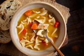 Bowl of chicken noodle soup with a spoon and bread on the side