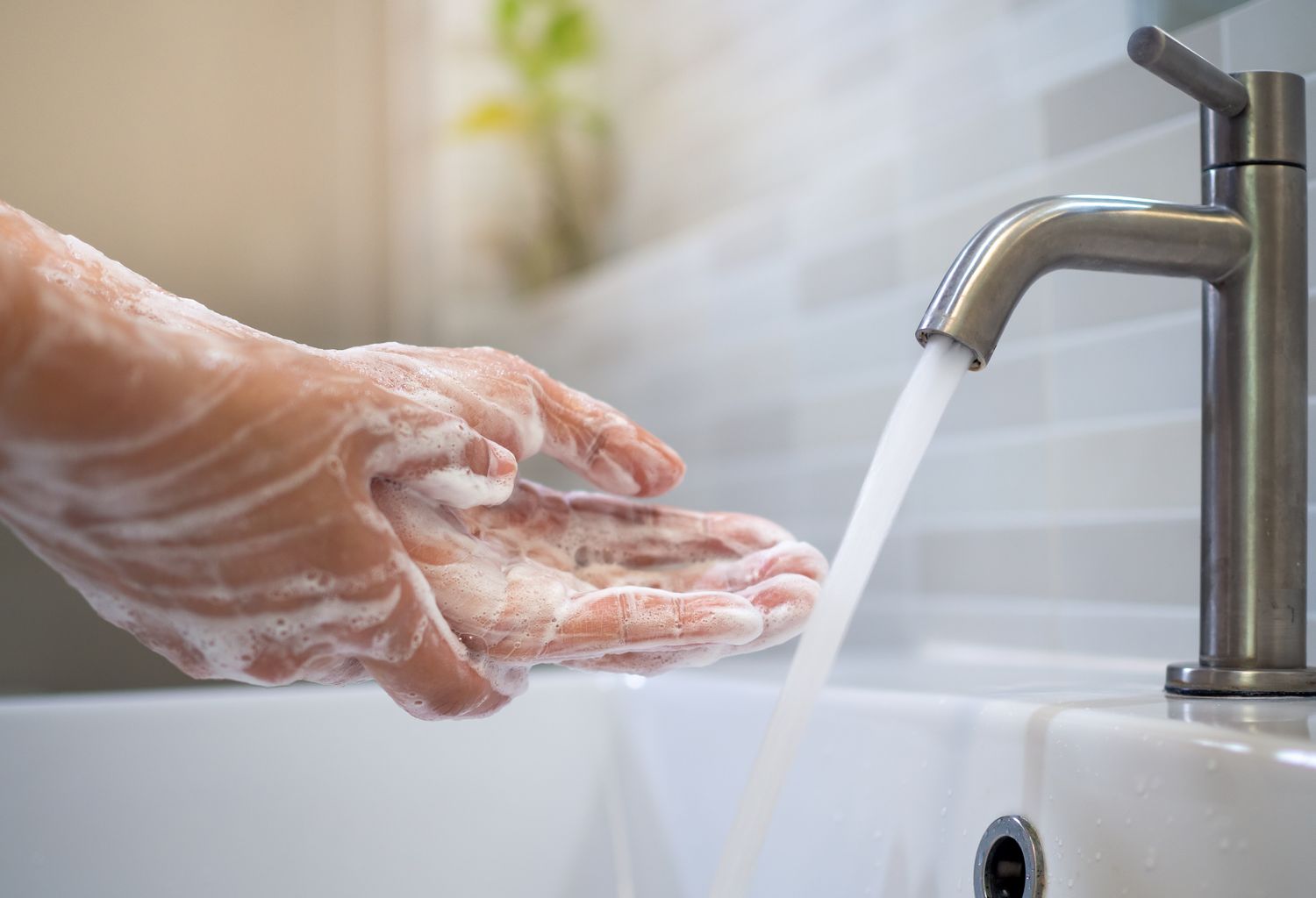 Hands being washed under running water from a faucet with soap lathered on the skin
