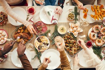 People reaching for food and drinks at a festive dinner gathering surrounded by various holiday dishes