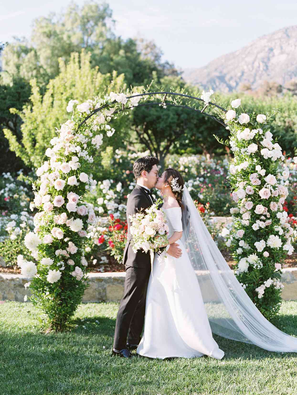 wedding couple first kiss under floral ceremony arch
