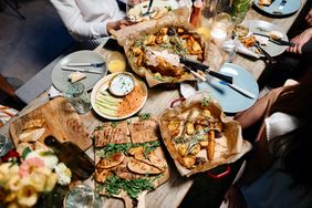 A table set with plates of food including roasted vegetables grilled meats and dips with people seated around it