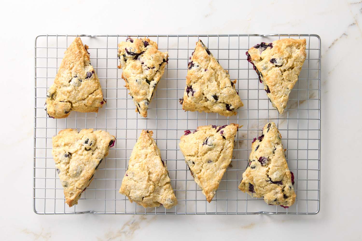 Eight blueberry scones arranged on a cooling rack on a white background