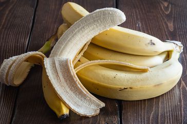 Several bananas, one partially peeled, on a wood surface