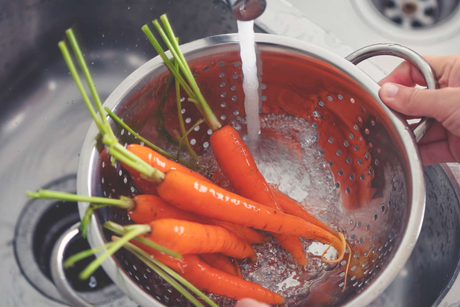 Carrots being rinsed in a colander under running water