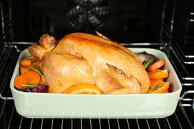 A cooked whole chicken in a baking dish with vegetables in an oven