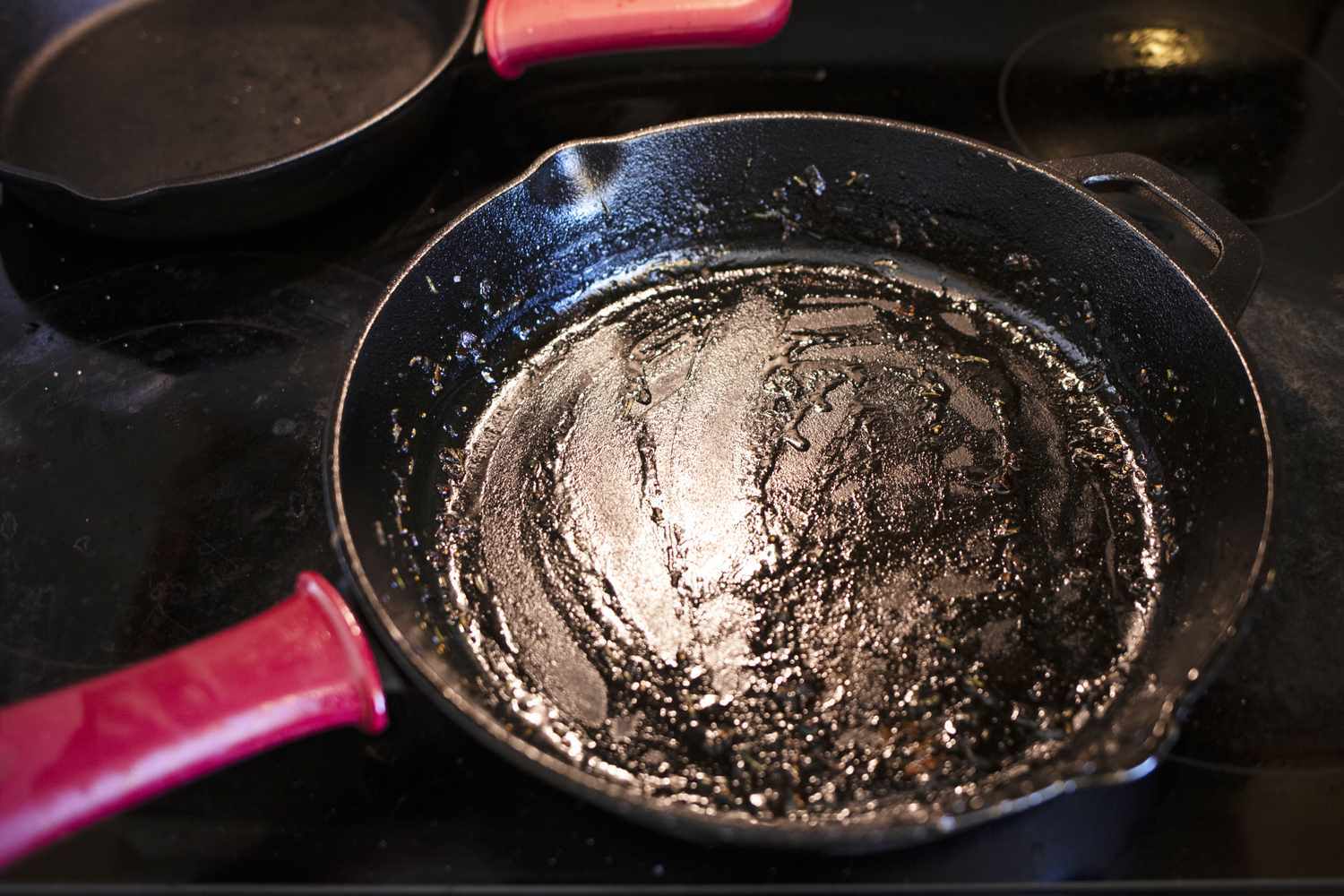 A used frying pan with a red handle on a stovetop traces of grease visible inside the pan