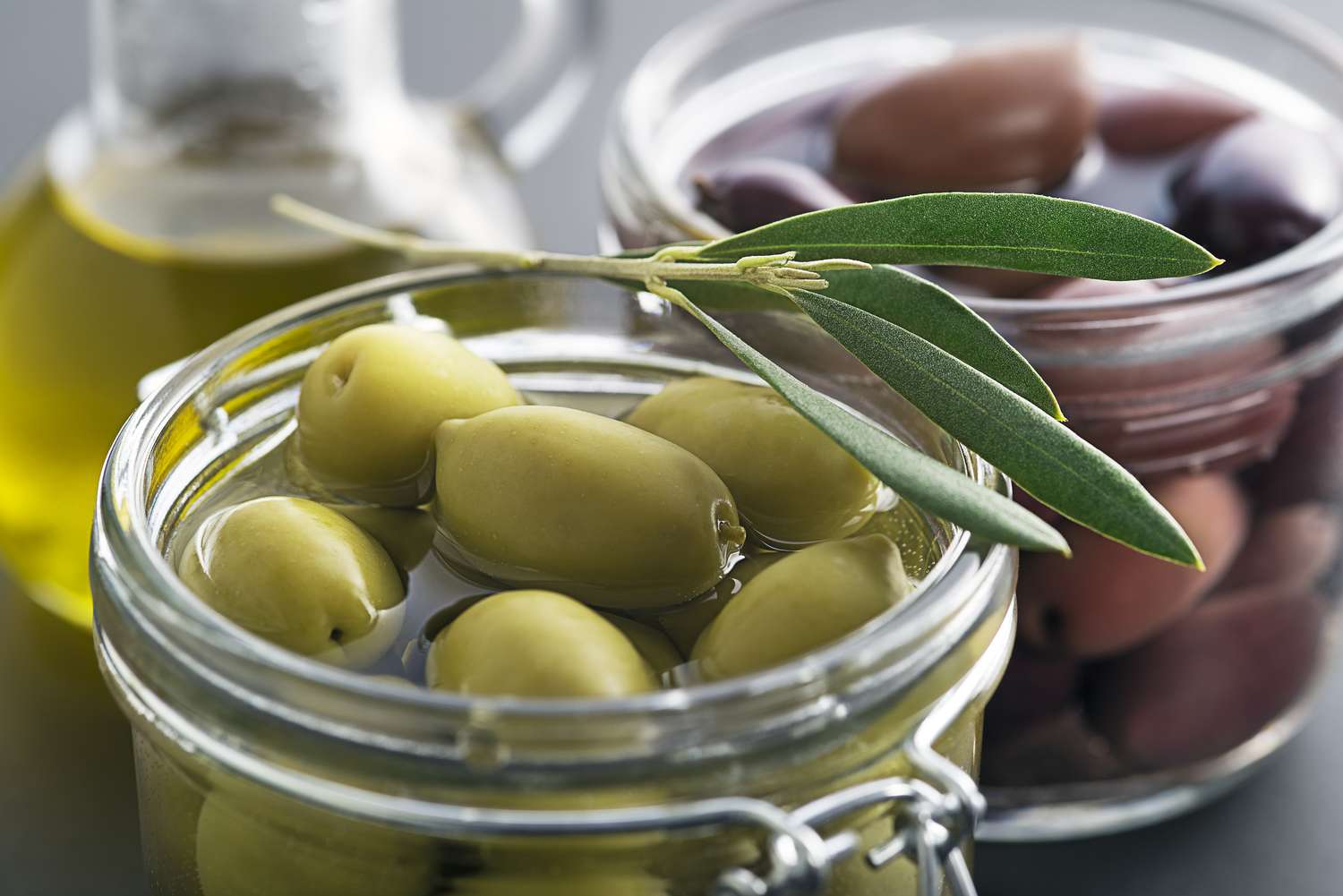 Jars of green and black olives a bottle of olive oil garnished with olive leaves