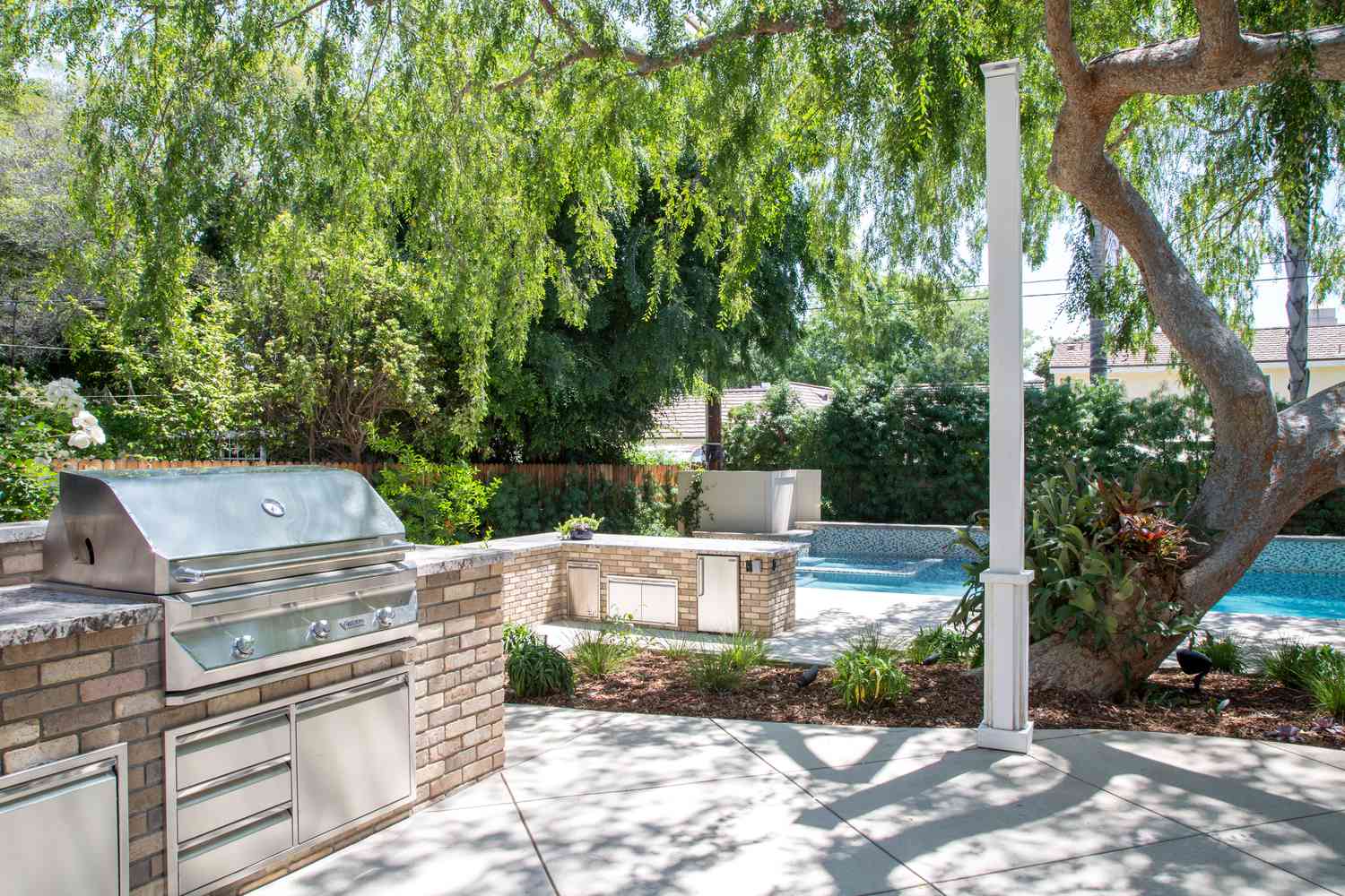 a brick outdoor kitchen with stainless steel appliances in front of a pool