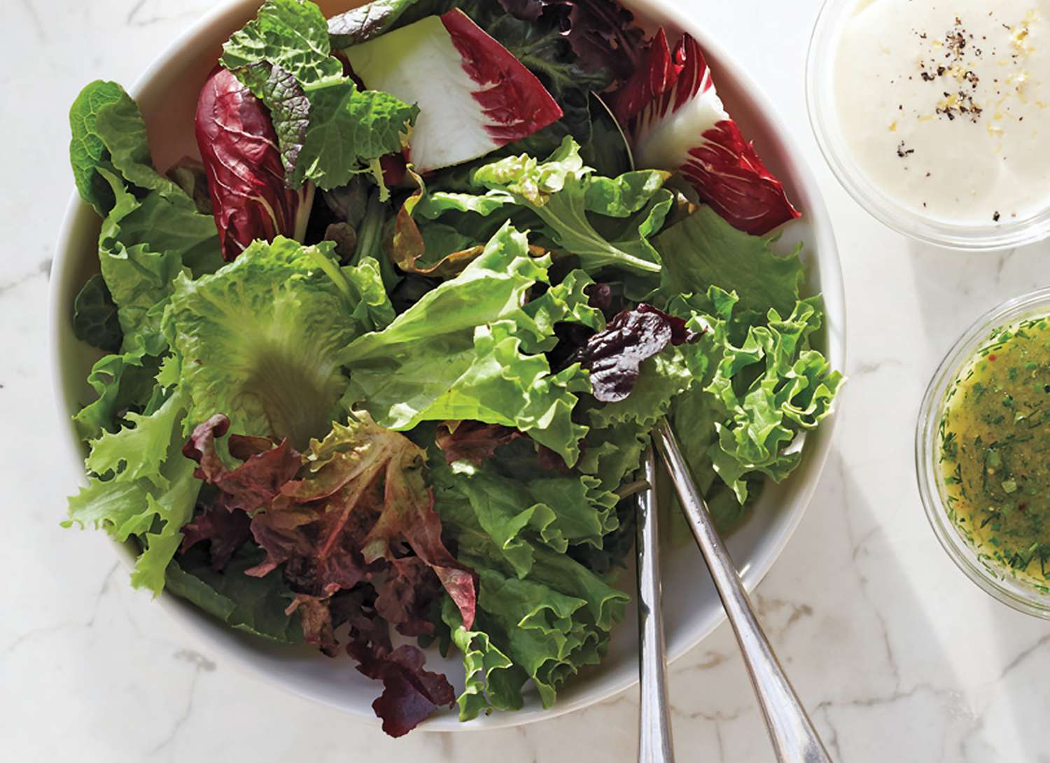 overhead view of bowl of lettuce with dressings on the side