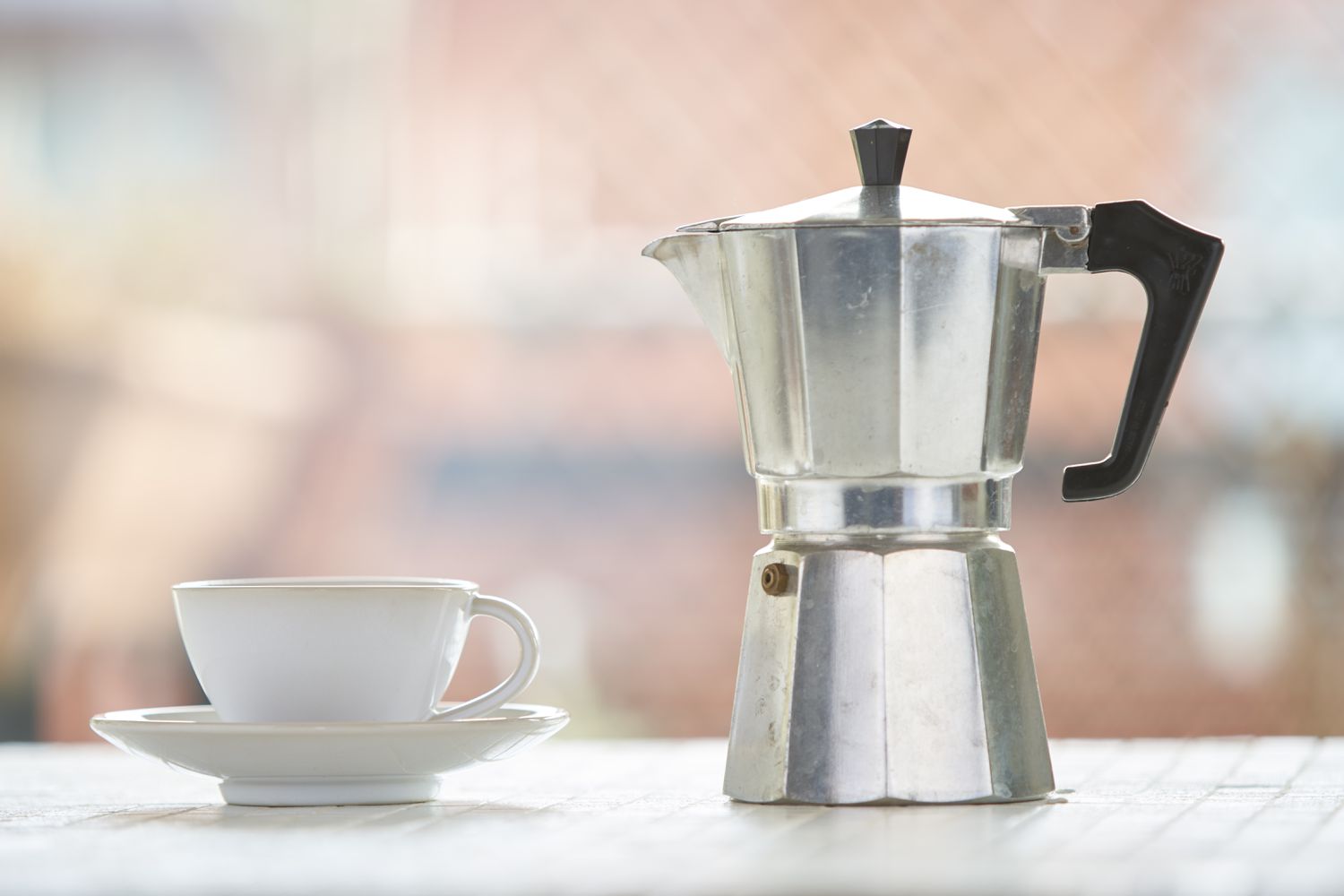 Moka pot and coffee cup against blurry background
