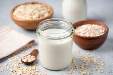 A jar of oat milk surrounded by bowls of oats