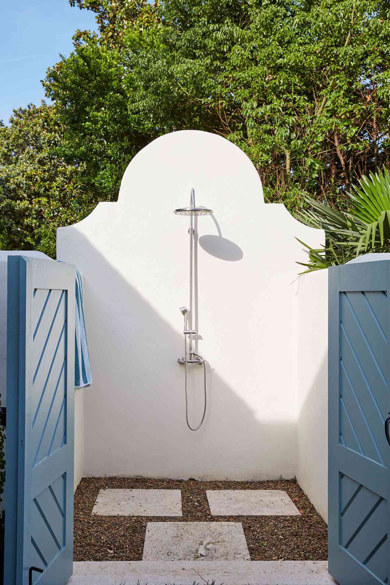 White outdoor shower with a pop of blue doors and lush greenery 