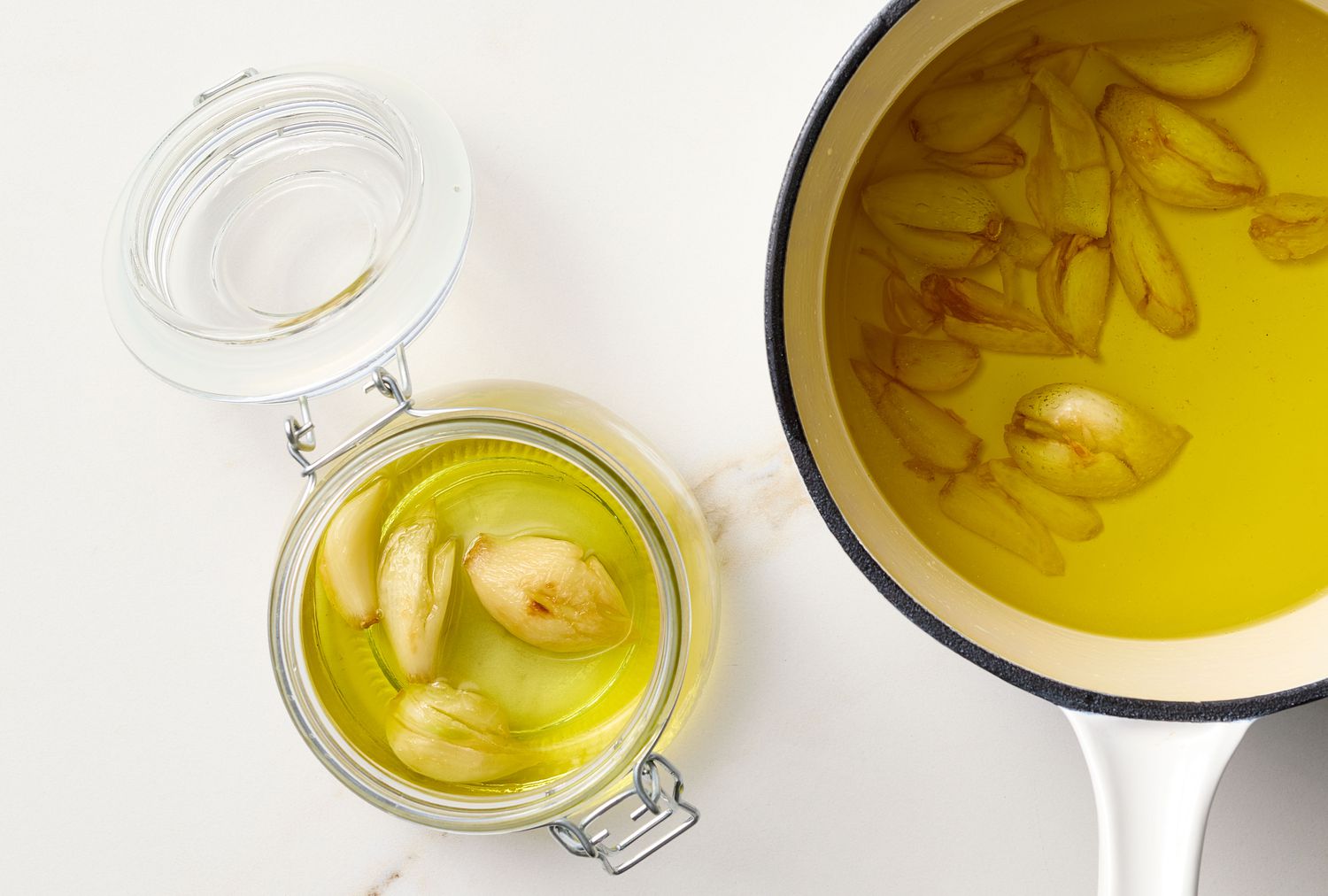 A pot and jar of garlic confit in oil, the garlic cloves are visible inside both vessels