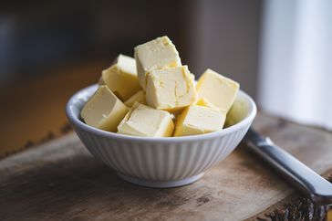 A bowl filled with cubes of butter on a wooden surface with a butter knife nearby