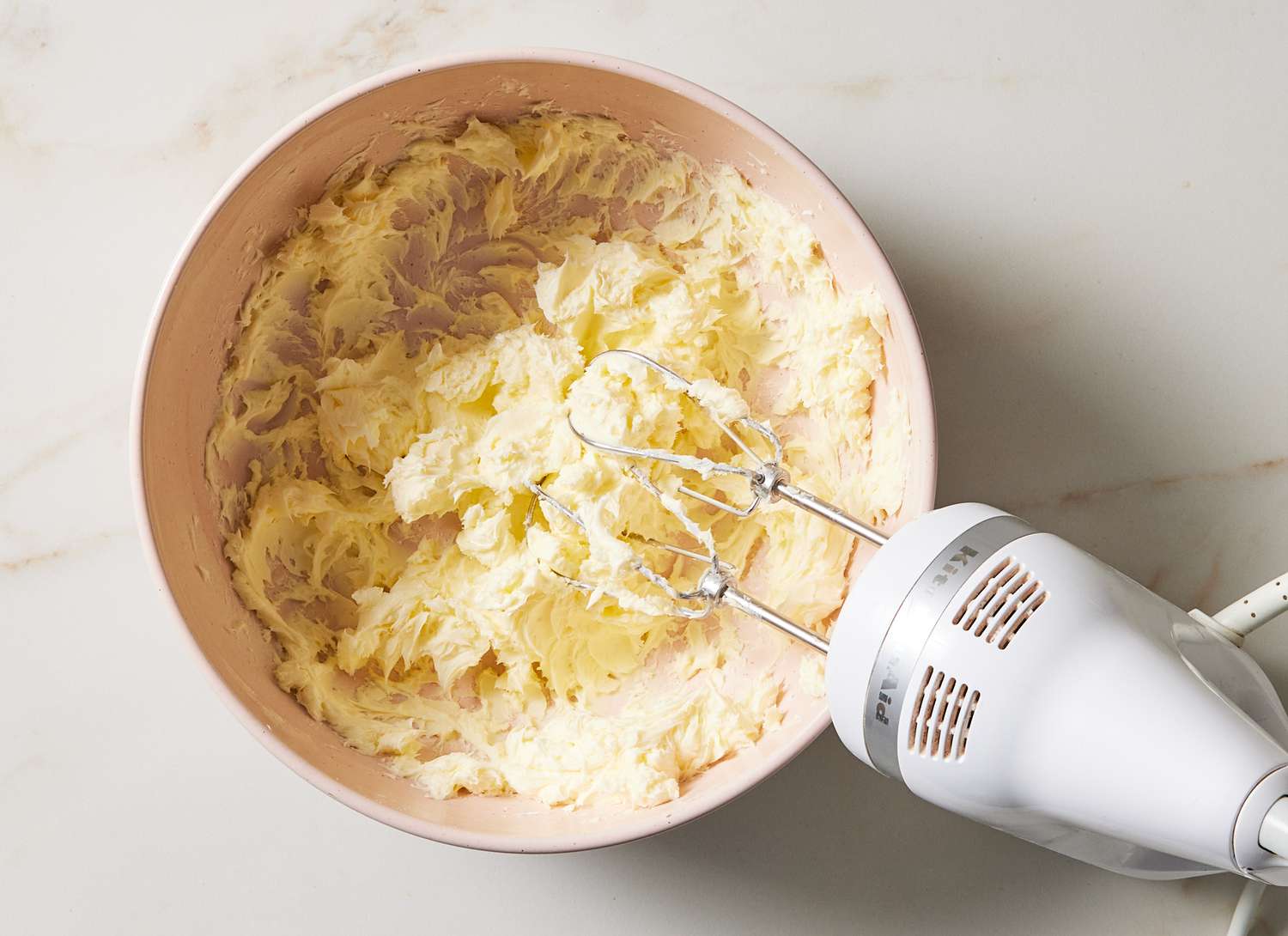overhead view of mixing bowl of white frosting and hand mixer
