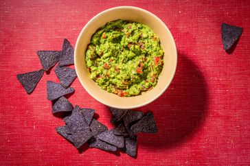 gucamole in bowl on red surface with purple tortilla chips