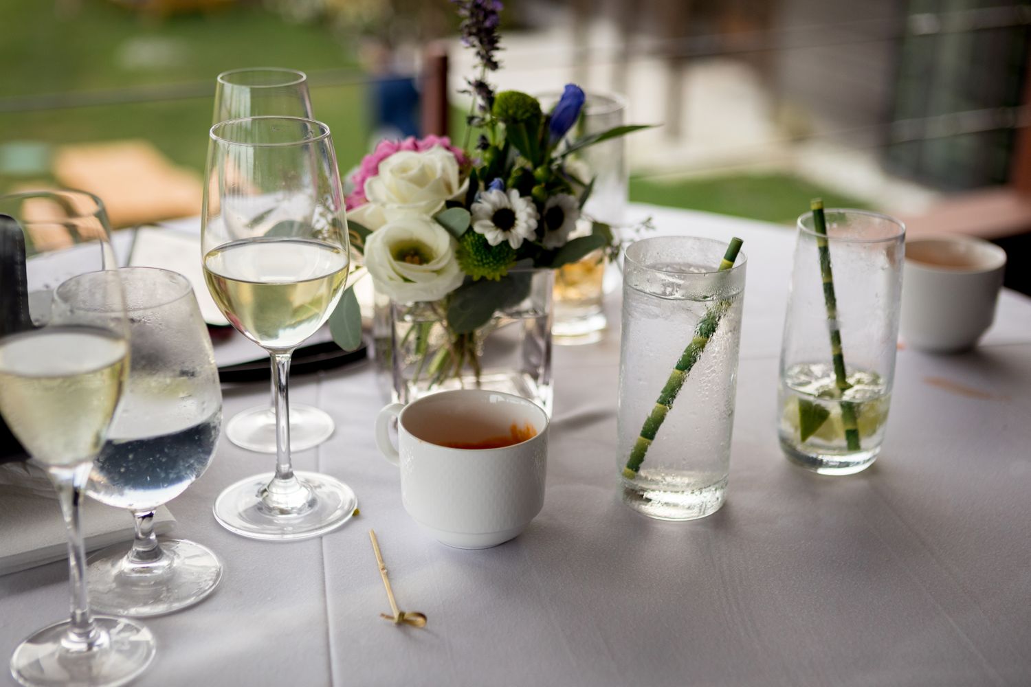 A set table with glasses of beverages a floral centerpiece and small dining items on a white tablecloth