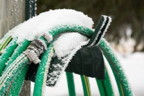 A coiled garden hose covered in snow and frost outdoors