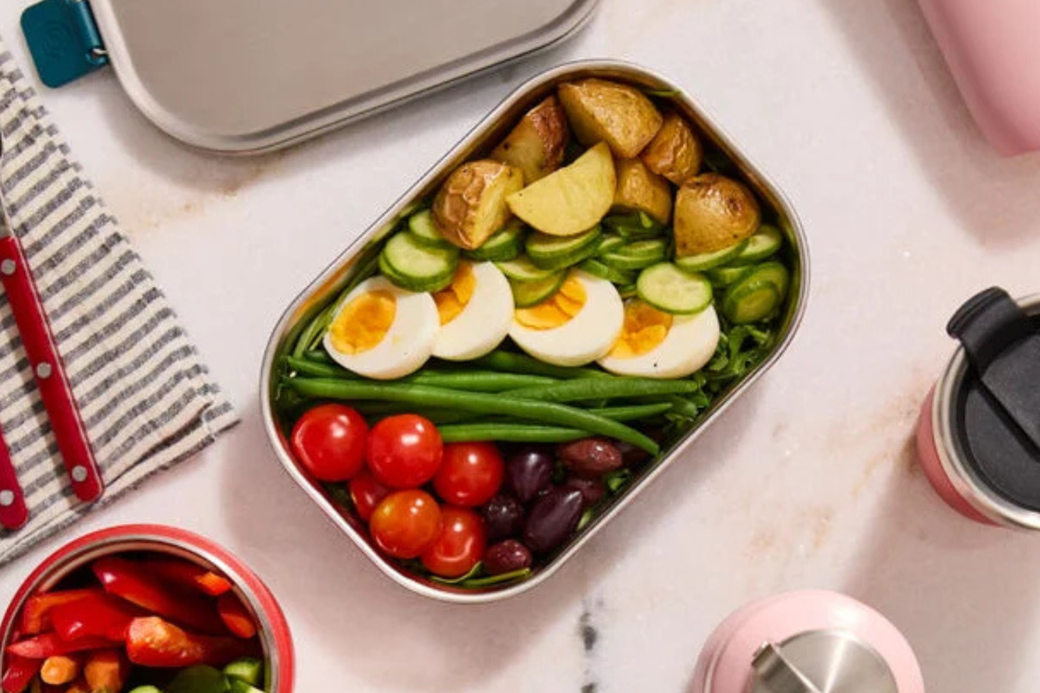 A packed lunchbox with eggs potatoes tomatoes cucumbers green beans and olives arranged methodically
