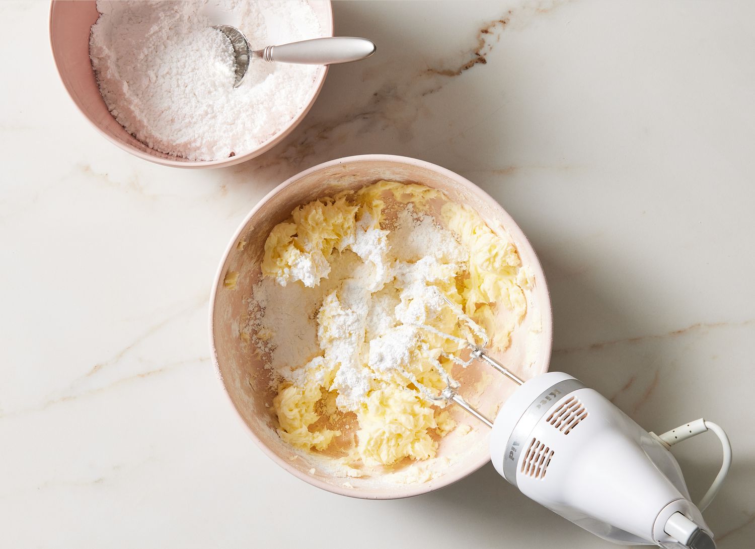 mixing bowl of white frosting & flour, hand mixer and bowl of flour