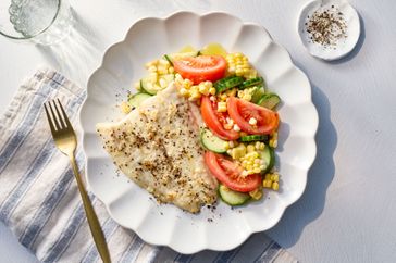 A plate with broiled fish and a summer salad with tomatoes, cucumbers, and corn
